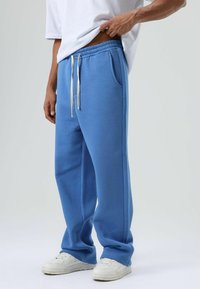 Blauwe joggingbroek van een katoenmix, met zijzakken, een elastische tailleband met trekkoorden en een losse pasvorm. Draagt wit sneakers.