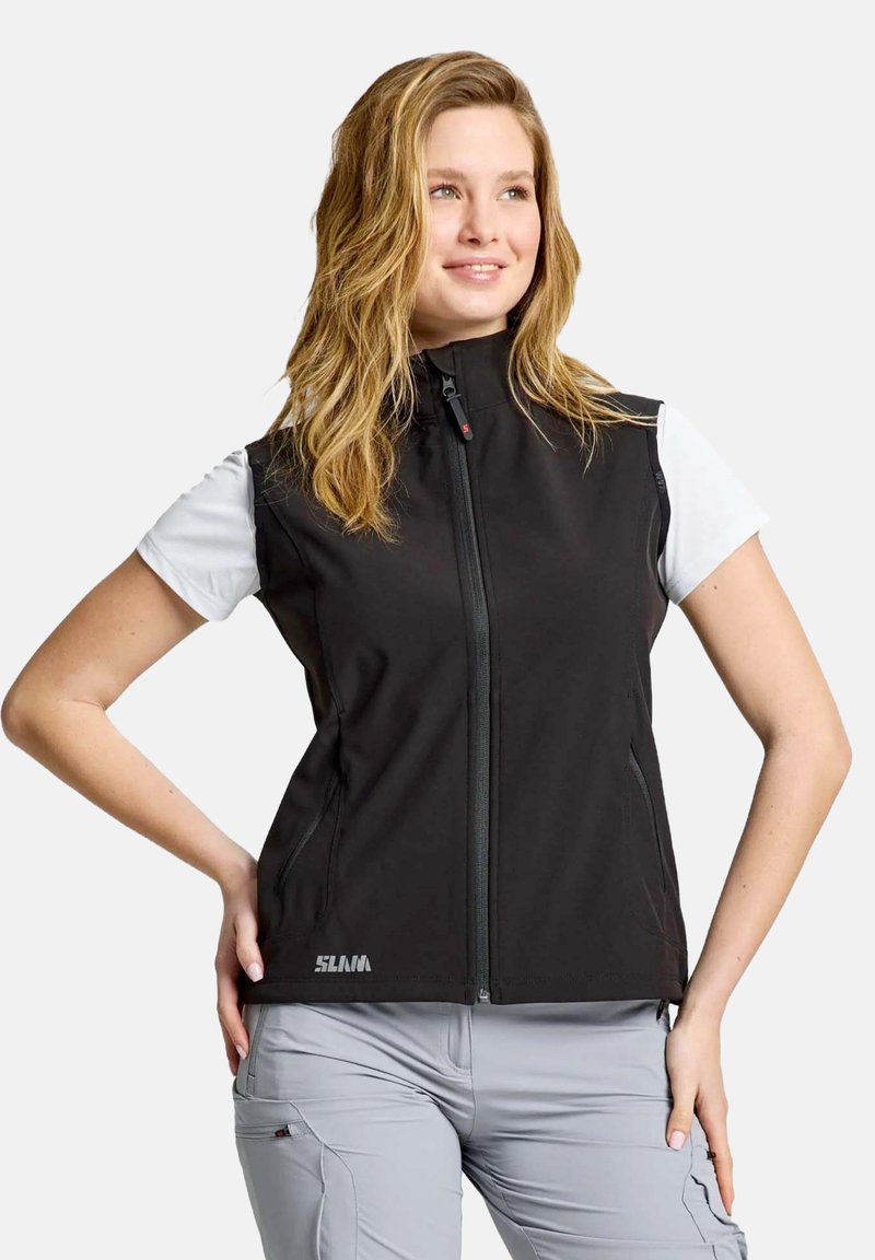 Schwarze ärmellose Weste mit hohem Kragen, Frontreißverschluss und Seitentaschen, getragen über einem weißen T-Shirt, kombiniert mit hellgrauen Hosen.