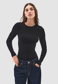 Maglietta nera a maniche lunghe a coste con scollatura rotonda e design aderente, indossata con jeans in denim blu scuro con tasche frontali.