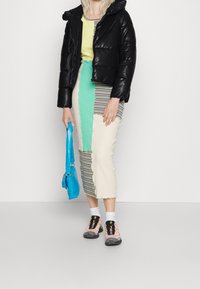 Doudoune noire, jupe midi rayée et en blocs de couleurs vert, crème et bleu. Sac à main bleu, chaussettes blanches et chaussures de sport colorées.