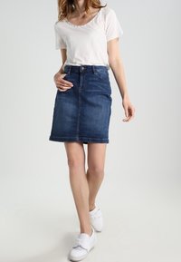 Jeansová sukně, tmavě modrá, po kolena, se rovného střihu a olemovaným okrajem. Kombinovaná s bílým tričkem s krátkým rukávem a bílými teniskami.
