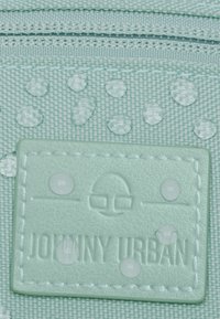 Hellgrüner Stoff mit Wassertropfen, der eine strukturierte Oberfläche aufweist. Ein rechteckiger Logo-Patch mit der Aufschrift "JOHNNY URBAN" ist eingeprägt und genäht.