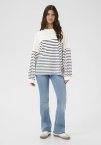 Long-sleeve striped sweatshirt in cream and navy. Features a relaxed fit with ribbed cuffs. Paired with light blue flared jeans and white sneakers.
