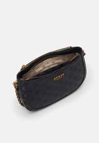 Černá crossbody kabelka Guess s raženým logem, zlatým řetízkovým popruhem a dvěma zipovými přihrádky, které ukazují béžovou podšívku s logem.
