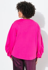 Sudadera de gran tamaño en fucsia con mangas largas abullonadas, que presenta un cuello redondo y una textura suave, combinada con leggings brillantes de lentejuelas.