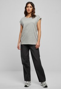 Maglietta grigia a maniche corte in tessuto morbido, abbinata a jeans di denim scuro a taglio largo e scarpe sportive argentate.