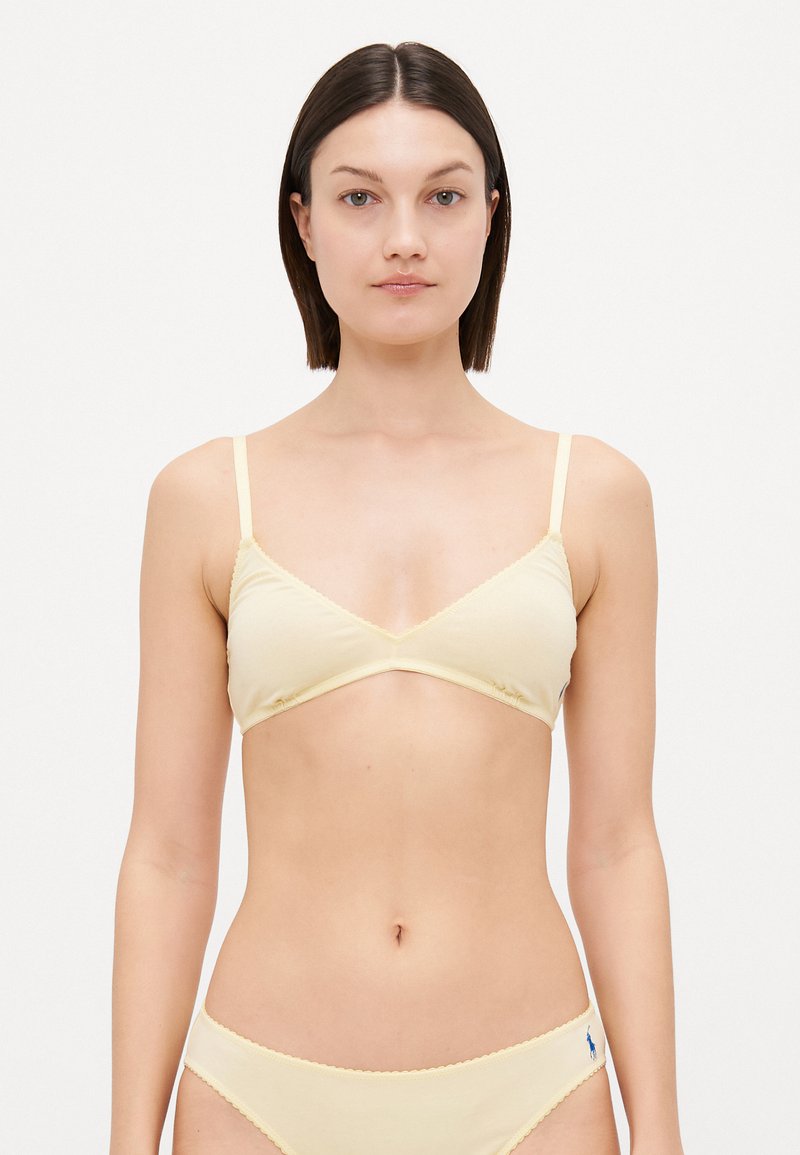 Dzeltena kokvilnas bralette ar trīsstūra formu, regulējamiem siksniņām un viļņotām malām. Saskaņota ar atbilstošām frillētām bikini apakšbiksēm.