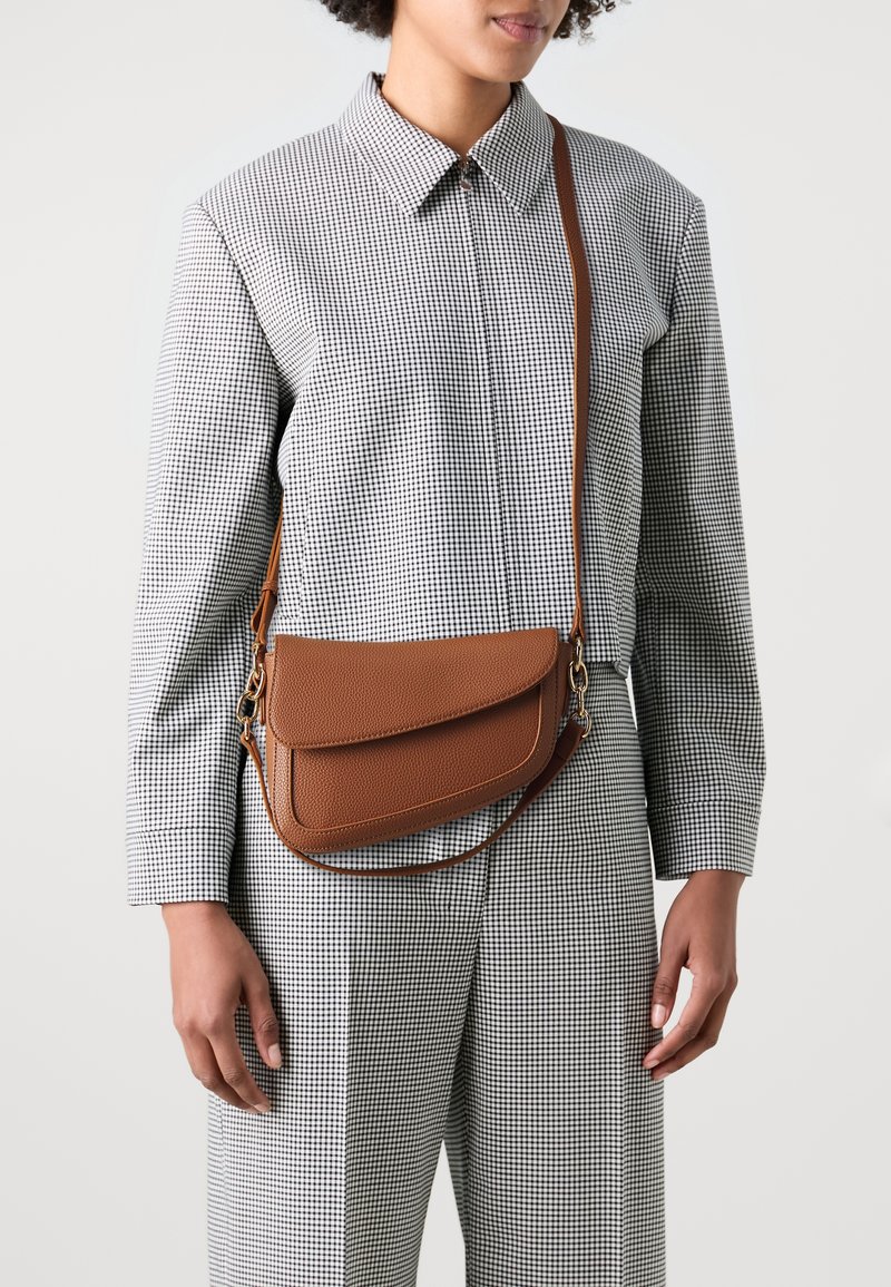 Sac bandoulière en cuir marron avec une surface texturée et une fermeture à rabat, doté d'une longue bandoulière réglable et d'accents métalliques.