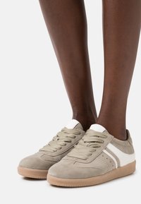 Sneakers in suede grigio chiaro con dettagli bianchi, punta rotonda, suola in gomma beige spessa e lacci testurizzati. Design a strisce laterali con perforazioni.