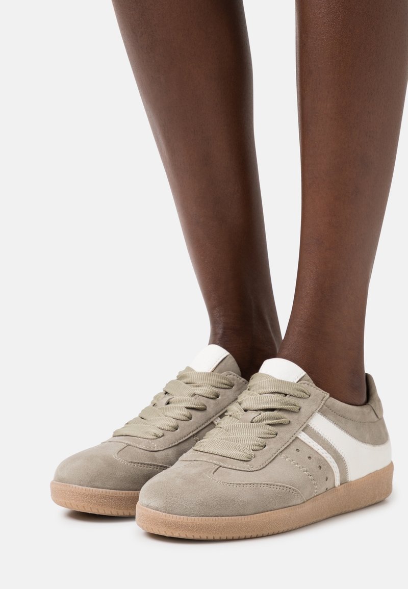 Sneakers in suede grigio chiaro con dettagli bianchi, punta rotonda, suola in gomma beige spessa e lacci testurizzati. Design a strisce laterali con perforazioni.