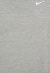 Camiseta de manga corta de color gris claro, hecha de tela suave, con cuello redondo y un logo blanco de Nike en el área izquierda del pecho.