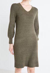 Abito a maglia verde oliva con scollatura a V, maniche lunghe a sbuffo, texture a costine e una silhouette aderente che si stringe leggermente all'orlo.