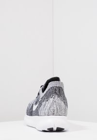 Scarpa atletica a maglia in bianco e nero con tomaia tessurizzata, silhouette bassa e suola bianca con un accento nero sul tallone.