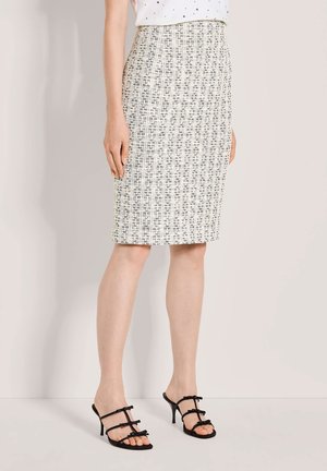 Frau trägt einen knieumspielenden Rock aus Tweed mit hohem Bund und schwarz-weißem Muster, kombiniert mit schwarzen, geschnürten High-Heels.