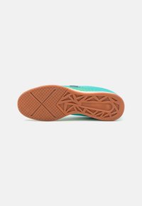 Suela de zapato deportivo con una superficie de goma texturizada, de color marrón claro y con un patrón geométrico y un diseño de logo en el centro.