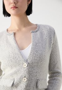 Knopen cardigan in een visgraatpatroon, met een lichtgrijze kleur, zachte textuur, ronde halslijn en twee voorzakken.