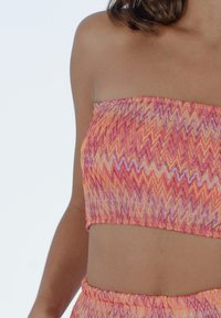 Top bandeau senza spalline con un motivo a zigzag in tonalità di rosa, arancio e bianco. Realizzato in un materiale testurizzato con un design aderente.