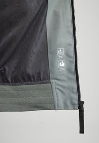 Windproof and water-repellent jacket in dark grey with textured fabric, featuring a smooth light grey hem and labeled care symbols.