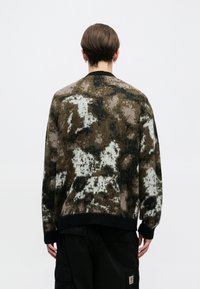 Smešani smešak i crn uzorak pulovera s opuštenim krojem, pletenom teksturom i crnim rebrastim ovratnikom i manžetama. Pogled s leđa.