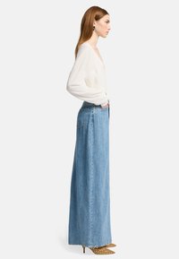 Maglione leggero di crema abbinato a una lunga gonna in denim blu, con vita alta e tasche laterali, indossato con scarpe col tacco gialle a pois.