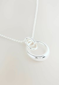 Collier en argent avec un pendentif comprenant des maillons ovale et circulaire interconnectés, au fini poli, suspendu à une chaîne délicate.