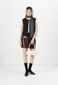 Gilet senza maniche a righe nere, top bianco, gonna in pelle bordeaux scuro, sciarpa a pois, borsa crema, calze nere e scarpe a punta.