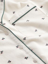 Chemise en coton avec un fond crème, imprimé de petites feuilles de houx vertes et de baies, passepoil contrastant vert foncé et boutons blancs.