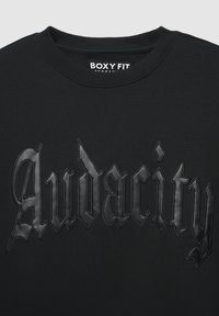Felpa nera con una vestibilità ampia, caratterizzata da un testo in rilievo "Audacity" in un font gotico sulla parte anteriore. Texture liscia e collo rotondo classico.