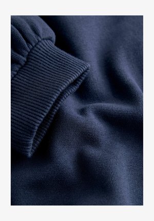 Navy blue, ribbed knit fabric with a soft texture. Features a gathered cuff and smooth, draping material. Detailed close-up view.