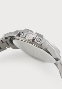 Relógio de aço inoxidável prateado com uma caixa arredondada, botões proeminentes e uma bracelete texturizada, apresentando um mostrador liso e refletor.