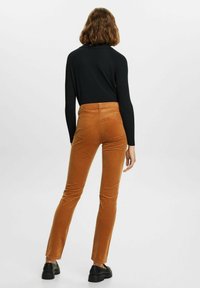 Brązowe spodnie typu corduroy w slim fit, z wysokim stanem i charakterystycznym pionowym prążkowaniem. Stylizowane z czarną, długą bluzką i czarnymi butami.