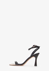 Sort højhælet sandal med et slankt stropdesign, der har en glat læderfinish og en spids hæl. Justerbar ankelrem inkluderet.
