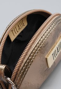 Primo piano di una pochette metallica bronzo parzialmente aperta con interno nero e etichetta del marchio T'LAISE su tessuto e piastra metallica.