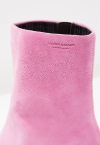 Rosa mockaskinnsankelboot med en mjuk textur, minimal sömnad och pr präglad "VAGABOND"-logotyp nära den övre kanten.