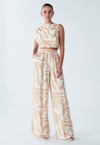 Gaismas divdaļīgs tērps ar bezroku tops un plaša piegriezuma bikses ar bēša un baltas abstraktas raksta. Mīksts, plūstošs audums.