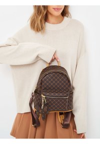 Zaino marrone a fantasia con dettagli in metallo dorato, forma arrotondata e rifiniture color cammello. Ha un piccolo charm attaccato e spallacci regolabili.
