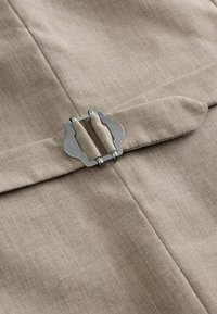 Ceinture en tissu beige avec boucle métallique argentée sur fond textile beige assorti, montrant les détails des coutures.