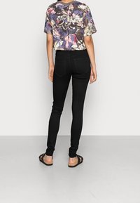 Jeans negros ajustados con cintura alta y bolsillos traseros, combinados con una blusa de manga corta con un patrón floral multicolor.