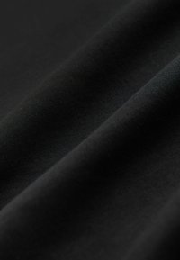 Tela negra con una textura suave, que presenta arrugas y pliegues sutiles, exhibiendo un acabado mate y un color uniforme en toda su superficie.