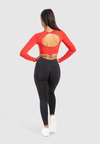 Rode cropped top met lange mouwen en een open rugontwerp, gecombineerd met high-waisted zwarte leggings, beide gemaakt van rekbare, strakke materialen.