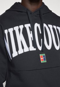 Sudadera negra con gran letra blanca "NIKE", cordones y un parche del logo de Nike multicolor en el frente. Material de mezcla de algodón, superficie texturizada.