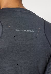 Sötétszürke sportpóló, texturált felülettel, világosszürke "ENDURA" felirattal. Apró perforációk a hátsó részen a szellőzés érdekében.