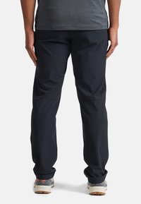 Pantalons légers bleu foncé avec une coupe décontractée. Dispose d'un tissu lisse, d'une taille élastique et de jambes fuselées. Portés avec des chaussures grises et crème.
