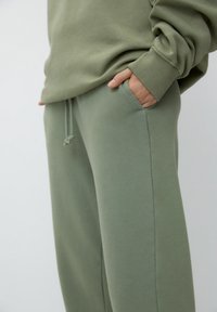 Olijfgroene sweatshirt en bijpassende sweatpants, gemaakt van zacht textiel. De sweatpants hebben een taille met trekkoord en zijzakken.