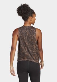 Top sin mangas marrón con un patrón de serpiente negra, con un corte relajado y dobladillo redondeado, combinado con leggings negros.