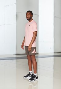 Camiseta corta de manga en rosa claro con un logo negro, combinada con pantalones cortos de color verde oliva con un acento rosa. Unos zapatos deportivos negros completan el look.