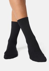 Sorte sokker lavet af et glat, elastisk stof med en ribbet kant, der sidder tæt om anklerne, uden mønstre eller designs.