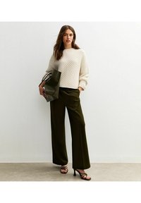 Maglione in tessuto avorio con collo a coste, abbinato a pantaloni larghi verde oliva a vita alta e sandali con tacco neri. Tiene una borsa scura.