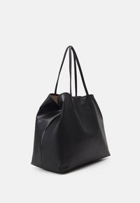 Borsa tote in pelle nera con una superficie morbida e testurizzata. Presenta manici lunghi e un design spazioso e morbido. Hardware e dettagli minimi.