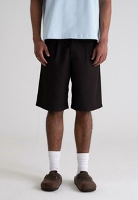 Black shorts with a relaxed fit, cotton material, and side pockets. Paired with a light blue shirt and brown clogs with white socks.